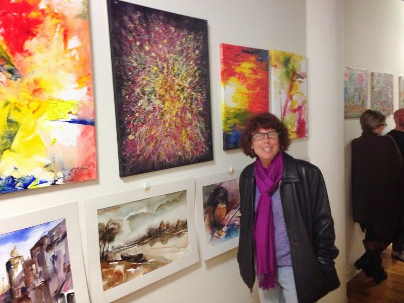 A visitor standing beside colorful abstract canvases and framed watercolors