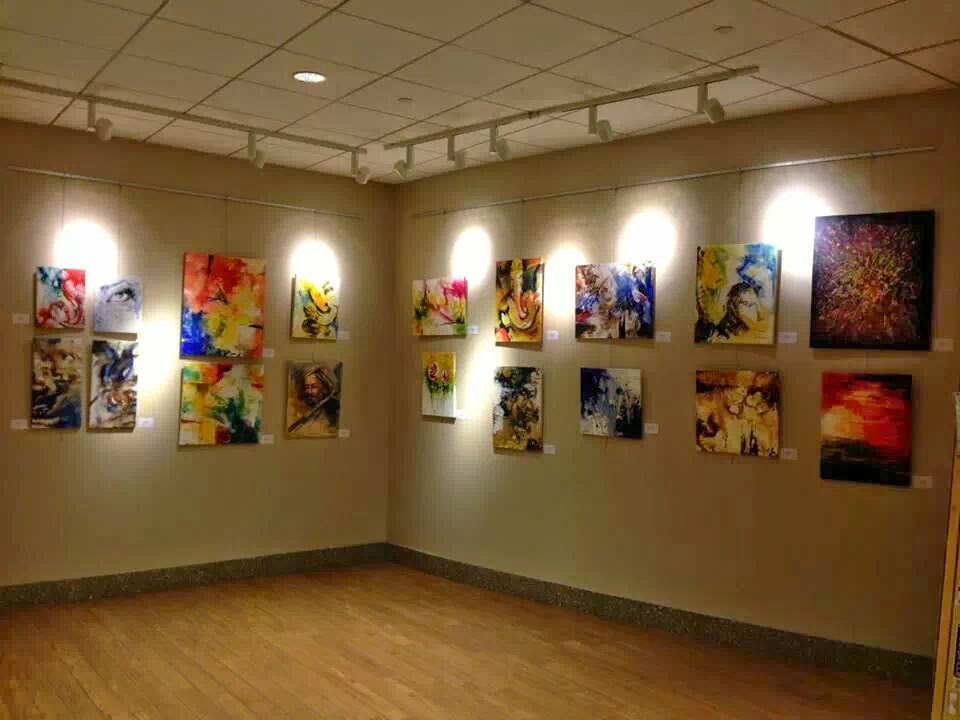 Corner of a gallery with abstract and figurative paintings under track lighting