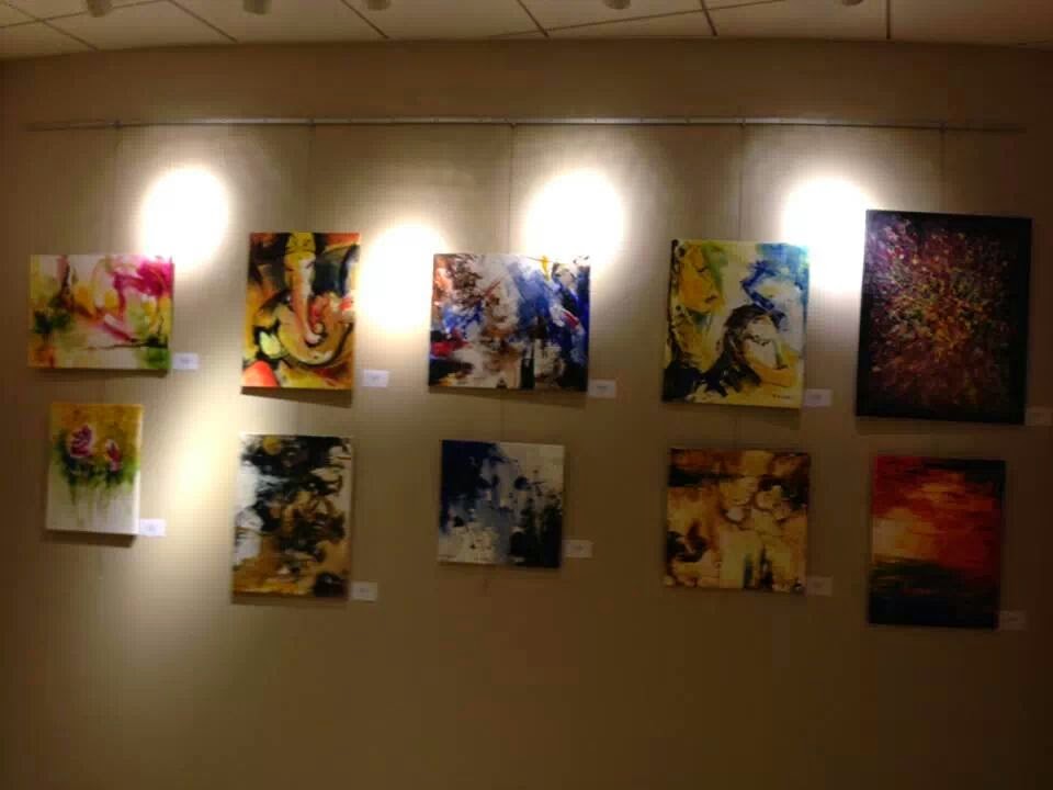 Ten paintings hung in two rows on a beige gallery wall